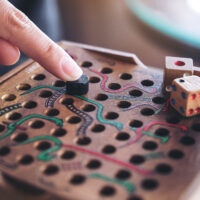 Closeup image of a hand playing wooden Snakes and Ladders game